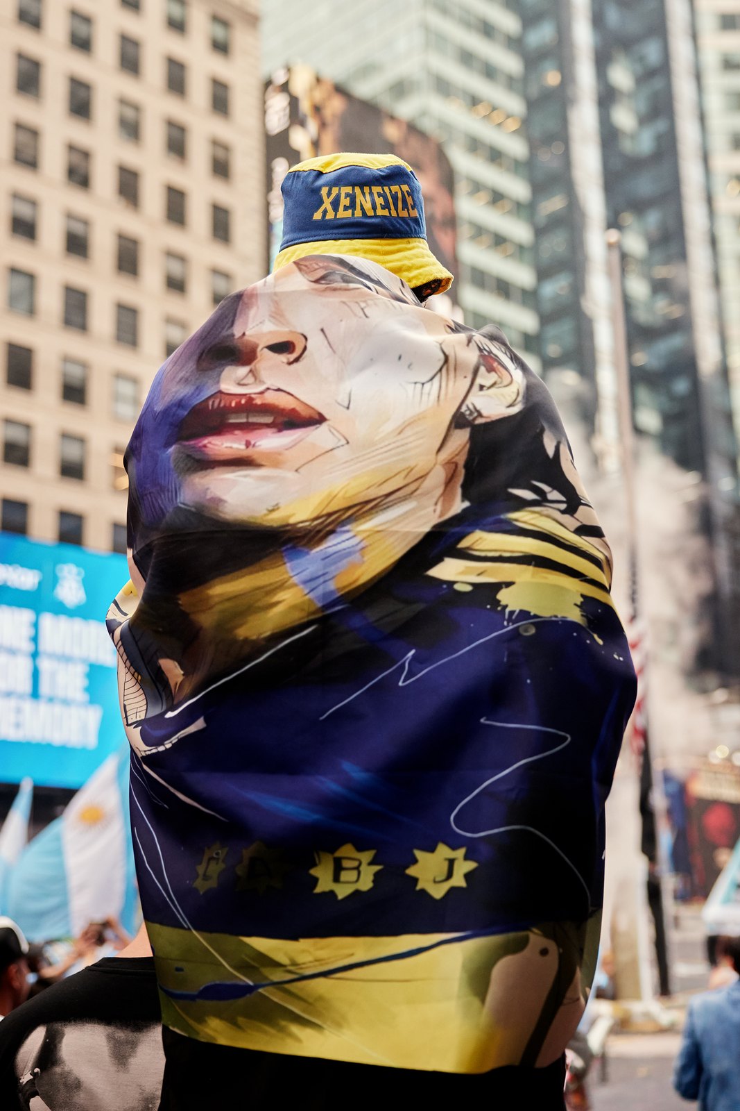 A fan wrapped in a blue and gold Xeneize flag wearing a Maradona mask on Seventh Avenue